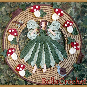 May include: A crocheted fairy with green and brown wings and a green dress, surrounded by mushrooms and leaves. The fairy is standing on a brown and beige crocheted circle with the text "BellaCrochet" at the bottom.