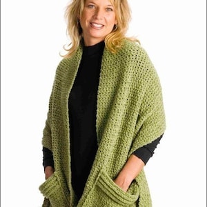 May include: A green crocheted shawl with pockets. The shawl is draped over a person's shoulders and the pockets are visible.