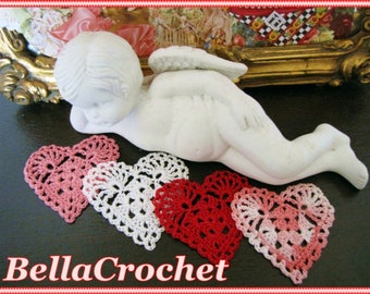Peut inclure: Cinq cœurs en crochet de couleur rose, blanc et rouge. Les cœurs sont disposés en rangée sur une surface sombre. Une figurine de chérubin blanc est couchée sur la surface derrière les cœurs.