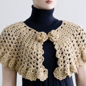 May include: A beige crocheted shawl with a scalloped edge and two flower-shaped buttons.