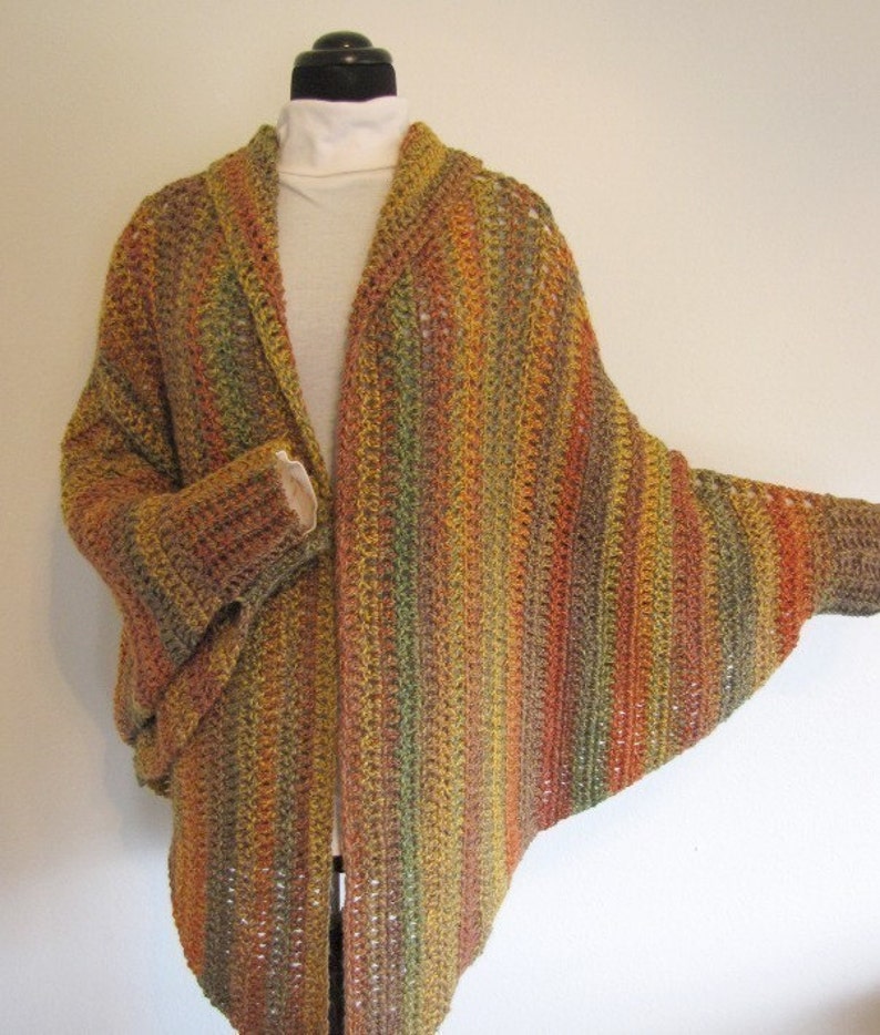 Op de afbeelding: Een gebreid vest met een losse pasvorm en lange mouwen. Het vest is gemaakt van een veelkleurig garen in tinten bruin, oranje en groen.