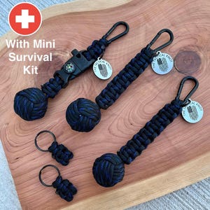 May include: Three black and blue paracord keychains with a small compass and a metal tag that says "The Tactical Knot". Each keychain has a knotted ball at the end.