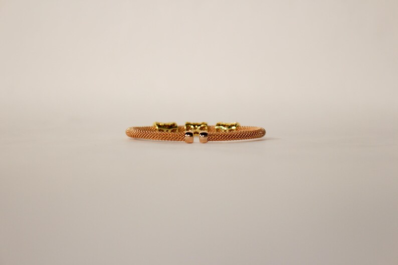 Unique golden mesh bracelet, adorned with vibrant crystals for a pop of color. The three meticulously crafted crystal-encrusted cylindrical accents create a perfect balance of elegance and modern style. Lightweight and comfortable for versatile use.