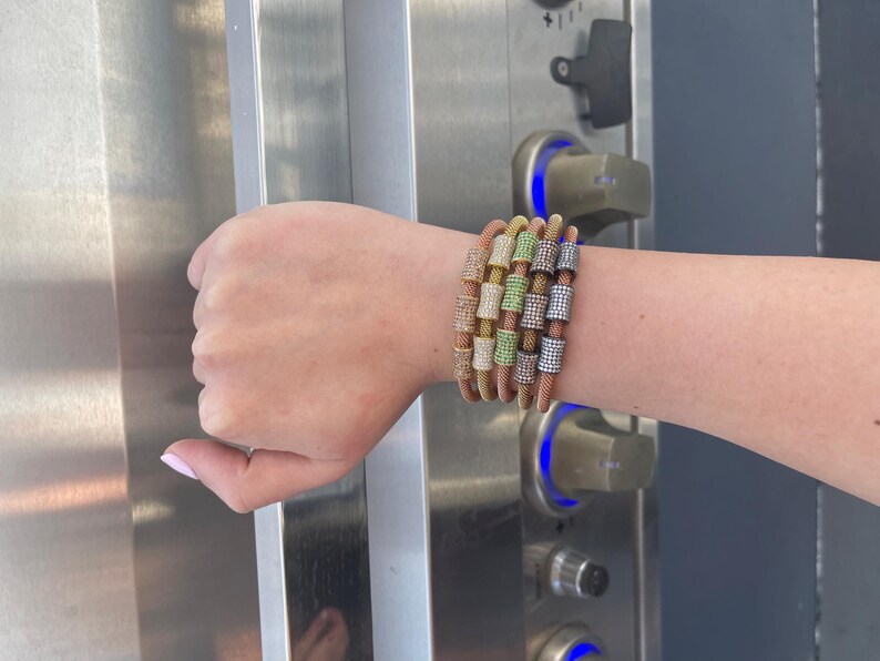 Unique golden mesh bracelet, adorned with vibrant crystals for a pop of color. The three meticulously crafted crystal-encrusted cylindrical accents create a perfect balance of elegance and modern style. Lightweight and comfortable for versatile use.