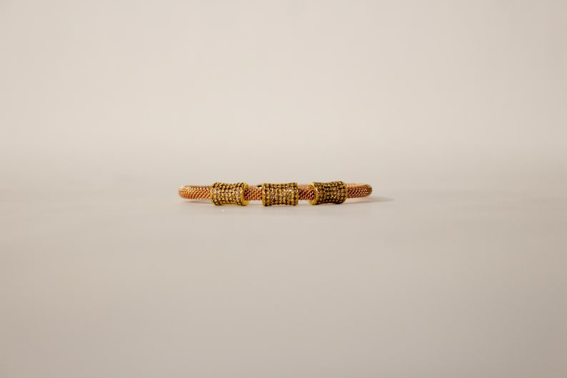 Unique golden mesh bracelet, adorned with vibrant crystals for a pop of color. The three meticulously crafted crystal-encrusted cylindrical accents create a perfect balance of elegance and modern style. Lightweight and comfortable for versatile use.