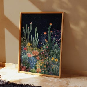 Pode incluir: Uma impressão artística emoldurada com uma ilustração vibrante de uma paisagem desértica. A obra de arte apresenta uma variedade de cactos e flores do deserto em tons de verde, amarelo, rosa e azul contra um céu noturno azul escuro com estrelas. A moldura é de madeira clara.