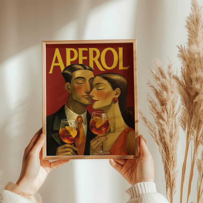 May include: A framed print featuring a vintage-style illustration of a couple holding Aperol cocktails. The artwork has a red background with the word "APEROL" in yellow. The couple is depicted with closed eyes, and the man is wearing a suit and tie.