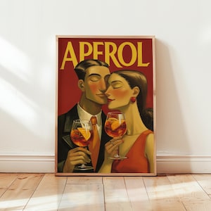 May include: A framed art print featuring a couple holding Aperol cocktails. The artwork has a vintage style with the word "APEROL" in yellow. The couple is depicted in a romantic embrace, with the woman in a red dress.