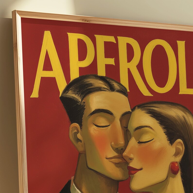 May include: A framed art print featuring the word "APEROL" in yellow letters against a red background. The artwork depicts a man and woman with closed eyes, their faces close together. The frame is made of light-colored wood.