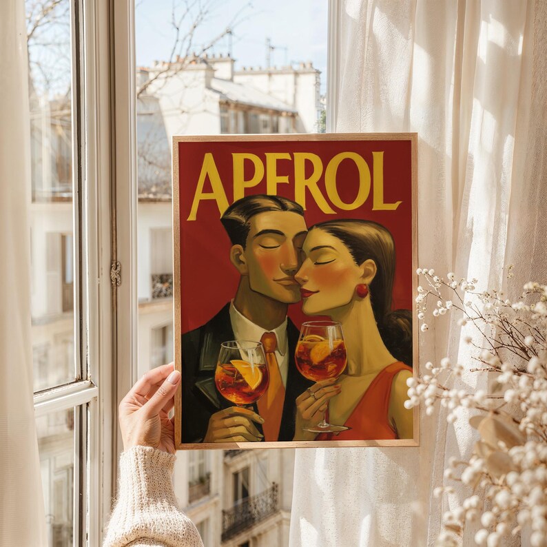 May include: A framed art print featuring a couple with closed eyes, holding Aperol cocktails. The artwork has a red background with the word "APEROL" in yellow. The man wears a black suit and the woman wears a red dress.