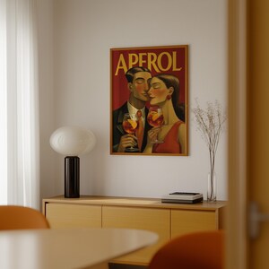 May include: A framed art print featuring a couple holding Aperol cocktails. The artwork has a vintage style with the word "APEROL" in yellow letters at the top. The couple is dressed in formal attire and the background is red.