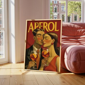 May include: A framed vintage-style print featuring a couple holding Aperol cocktails. The artwork has a red background with the word "APEROL" in large yellow letters. The couple is depicted with closed eyes, and the woman wears a red dress.