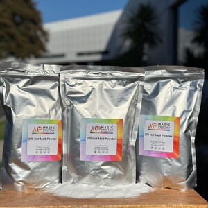 May include: Three silver foil bags of DTF Hot Melt Powder, labeled with the Magic Print4U logo. The bags are sitting on a wooden surface.