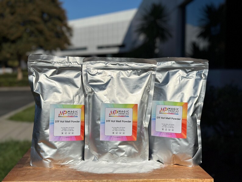 May include: Three silver foil bags of DTF Hot Melt Powder, labeled with the Magic Print4U logo. The bags are sitting on a wooden surface.