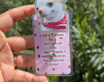 May include: A pink and white plastic badge holder with a cartoon chihuahua image. The badge holder has a silver glitter border and a clear plastic strap. The text on the badge holder reads: "high temperature places clean with soft cloths Avoid dropping continually or you may damage your product"