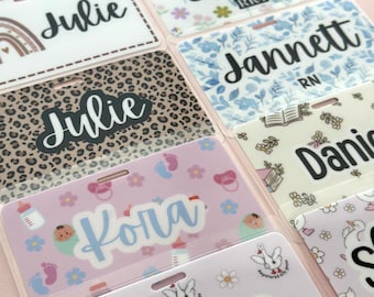 May include: A selection of personalised name badges with diverse designs. Some badges feature floral patterns, animal prints, and baby-themed graphics. Names such as "Megan," "Julie," and "Loagann" are displayed in different fonts.