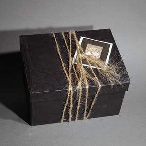 May include: A black gift box tied with twine and a small white card with a floral design. The card has the text "Happy Birthday" on it.