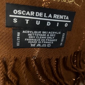 Pode incluir: Cachecol castanho e dourado com franjas. O r&oacute;tulo diz "Oscar de la Renta Studio" e inclui instru&ccedil;&otilde;es de cuidados em franc&ecirc;s e ingl&ecirc;s.