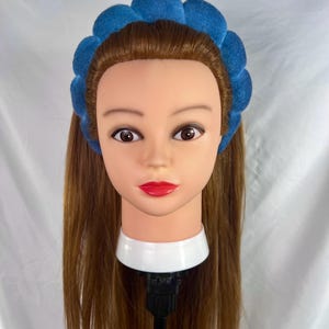 May include: A blue headband with a puffy, textured design. The headband is worn on a mannequin with long brown hair.