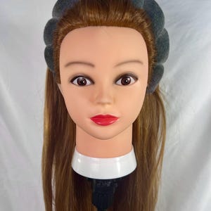 May include: A gray foam headband with a rounded shape, worn on a mannequin with long brown hair.