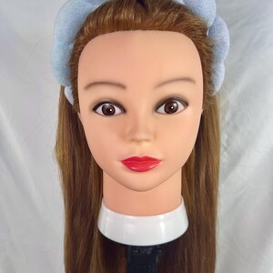 May include: A light blue headband with a puffy, textured design. The headband is made of soft fabric and is worn on a mannequin with long brown hair.