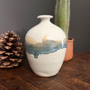May include: A white ceramic vase with a blue and brown glaze. The vase has a rounded body and a narrow neck.