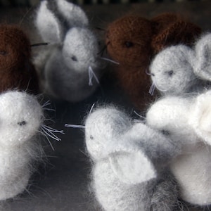 May include: A collection of handmade knitted bunny toys in various colors, including white, brown, and gray. The bunnies are made with soft, fluffy yarn and have long ears and sweet faces.