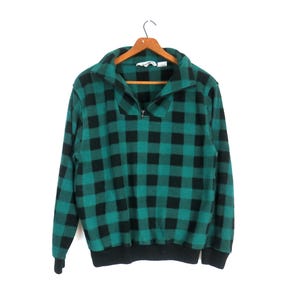 May include: Green and black plaid fleece pullover with a quarter zip closure. The sweater has a black ribbed collar, cuffs, and hem.