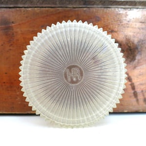 Op de afbeelding: Een doorzichtig plastic deksel met een zonnestralenontwerp en de letters "HR" in het midden.