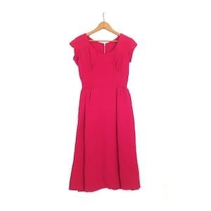 May include: A bright pink dress with a fitted bodice and a flared skirt, hanging on a wooden hanger. The dress features cap sleeves and a subtle scoop neckline. The fabric appears to be lightweight, suitable for warmer weather.