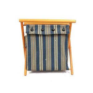 May include: A vintage wooden laundry hamper with a blue and gold striped fabric bag. The hamper has a natural wood frame and three black buttons on the top flap. The design is simple and functional, suitable for a bedroom or bathroom.