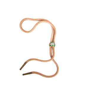 May include: A tan bolo tie with a round, colorful centerpiece featuring a landscape design. The cord is a braided texture, and the tips are capped with metal. This accessory is a classic piece of Western wear.