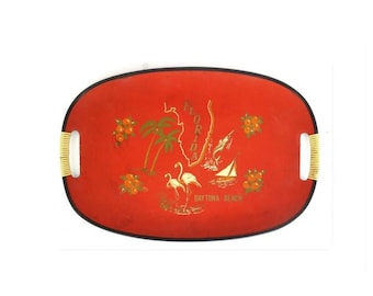 May include: Oval serving tray with a red background and a black border. The tray features gold illustrations of Florida, palm trees, oranges, flamingos, and a sailboat. The handles are white with gold accents. The text "Daytona Beach" is visible.
