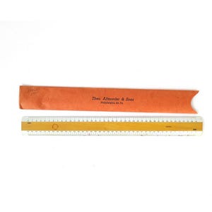 Puede incluir: Una regla de madera con marcas blancas y una funda de papel roja. La funda tiene el texto "Theo. Altshuler & Sons Philadelphia Pa."