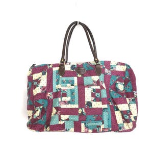 May include: A large patchwork tote bag with brown leather handles. The bag features a quilted design in shades of burgundy, teal, and cream, with floral patterns. It has two front pockets and a brown leather tag.