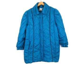 May include: A teal quilted coat with a button-up front and a collared neckline. The coat features vertical black trim and long sleeves. The coat is hanging on a wooden hanger against a white background.