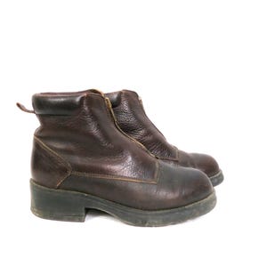 May include: A pair of brown leather ankle boots with a zipper closure. The boots have a rounded toe and a low, stacked heel. The leather appears worn, with visible creases and scuffs, suggesting they are well-used.