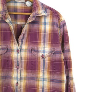 May include: A purple, yellow, and blue plaid button-down shirt with two chest pockets. The shirt is hanging on a wooden hanger against a white background. The plaid pattern is a mix of colors.