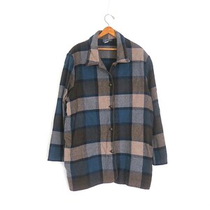 May include: A long-sleeve button-down jacket featuring a large plaid pattern in shades of dark blue, charcoal gray, and light beige. The garment has a classic collar, a straight hemline, and a front button closure, all displayed on a wooden hanger.