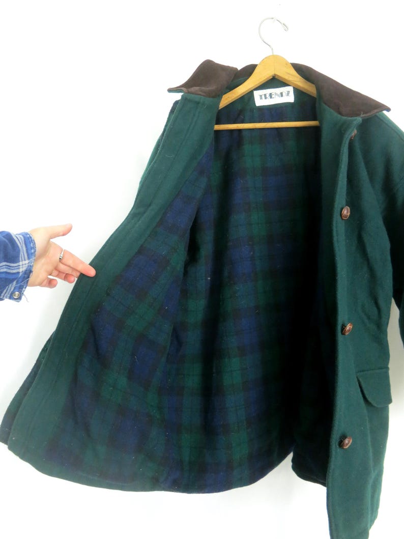 Puede incluir: Un abrigo de lana verde con cuello marr&oacute;n y forro a cuadros azul, verde y negro. El abrigo tiene botones marrones y una etiqueta que dice "TEENZ". Cuelga de una percha de madera.