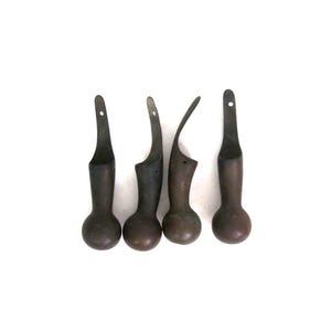 May include: Four dark brown metal furniture feet with a rounded ball base and a curved, upward-extending attachment plate. Each piece features a small circular hole at the top of the vertical extension for mounting purposes, showing a weathered finish.