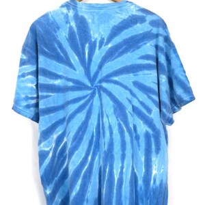 May include: A blue tie-dye t-shirt hanging on a wooden hanger. The shirt has a spiral pattern in shades of blue. The short-sleeved shirt is made of soft fabric. The design creates a visually striking effect.