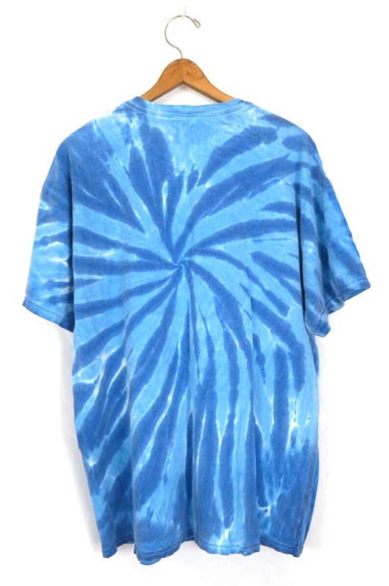 May include: A blue tie-dye t-shirt hanging on a wooden hanger. The shirt has a spiral pattern in shades of blue. The short-sleeved shirt is made of soft fabric. The design creates a visually striking effect.