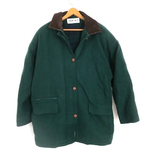 Puede incluir: Un abrigo de lana verde oscuro con cuello marr&oacute;n y botones de madera. El abrigo tiene dos bolsillos delanteros y un dise&ntilde;o cl&aacute;sico. El abrigo est&aacute; colgado de una percha de madera.