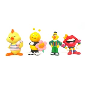 May include: A set of four small colorful figurines including a yellow chick in a striped shirt, a yellow bee holding a pink flower, a character with a yellow head in a striped shirt and green pants, and a red lips character with a yellow bow.