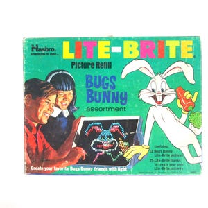 May include: Vintage Hasbro Lite-Brite picture refill set featuring Bugs Bunny. The box is green with the words "Lite-Brite" in yellow and pink. The box shows two children creating a Bugs Bunny picture with light. Includes 12 Bugs Bunny pictures.