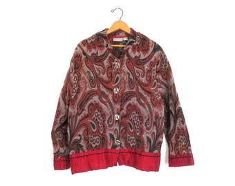 Könnte beinhalten: Knopfjacke mit Paisley-Muster in Rot-, Schwarz- und Grautönen. Die Jacke hängt an einem Holzbügel. Sie hat silberfarbene Knöpfe und einen roten Saum.