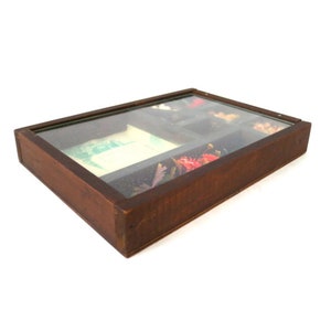 May include: A rectangular, wooden jewelry box with a glass top. The box is divided into compartments, some containing jewelry and small items. The wood has a dark brown finish, and the glass top allows a view of the contents.