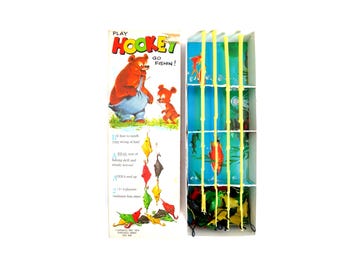 May include: Vintage Hookey Go Fishin' game in a box with a cartoon bear and a smaller bear holding a fishing rod. The box has a blue and green background with yellow fishing poles and colorful fish. The game is for ages 4 and up and includes 4 fishing poles, 2-4 players, and solitaire fun.