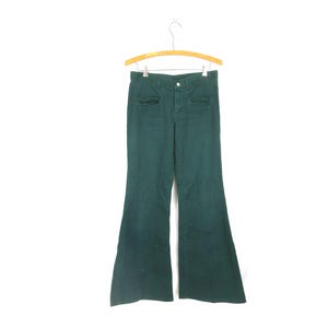Pode incluir: Calças largas de cor verde floresta escuro com cintura subida, fecho de botão frontal, braguilha com fecho de correr e dois bolsos horizontais nas ancas. As calças apresentam uma silhueta de perna larga que alarga a partir do joelho.